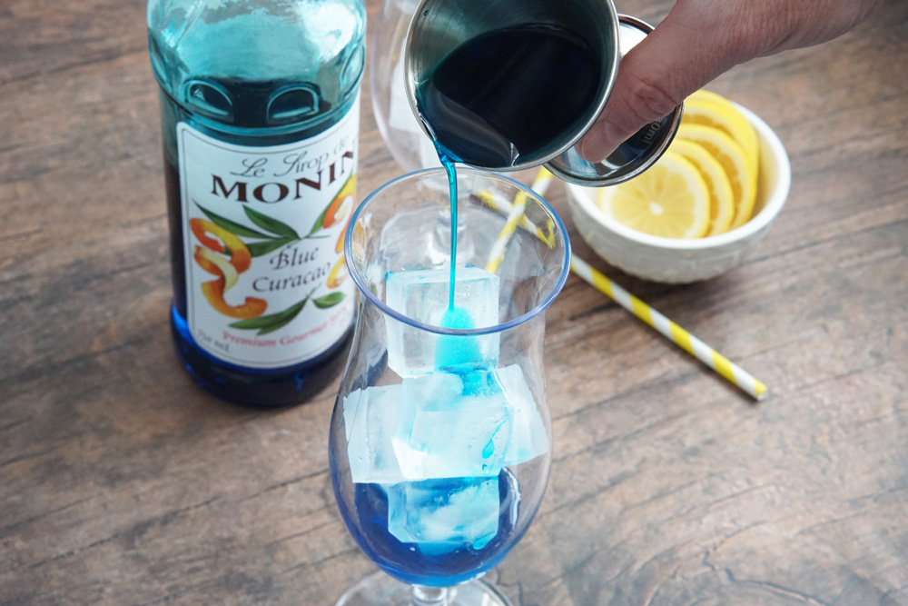 Pouring blue curacao into a hurricane glass