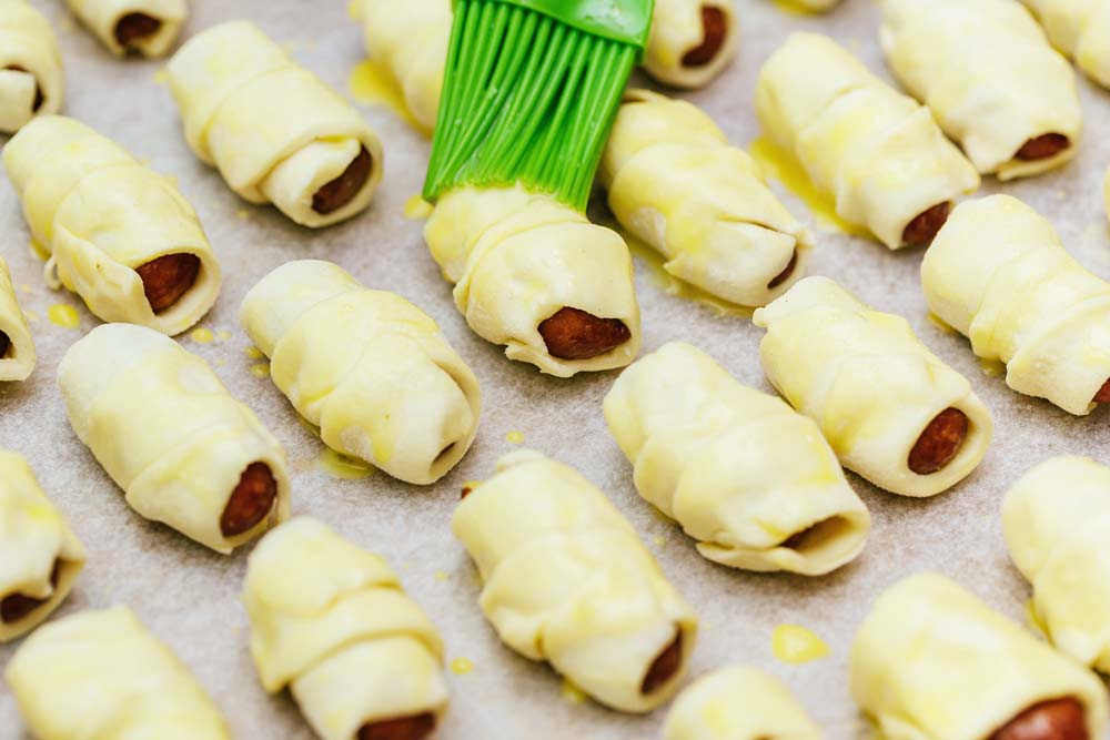 brushing uncooked pigs in a blanket with egg wash.